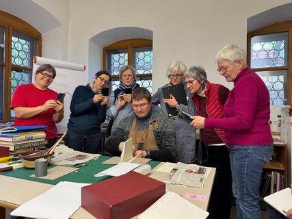 Vorführung Mehrere Personen stehen um einen Lehrer herum, der etwas an einem Buch zeigt